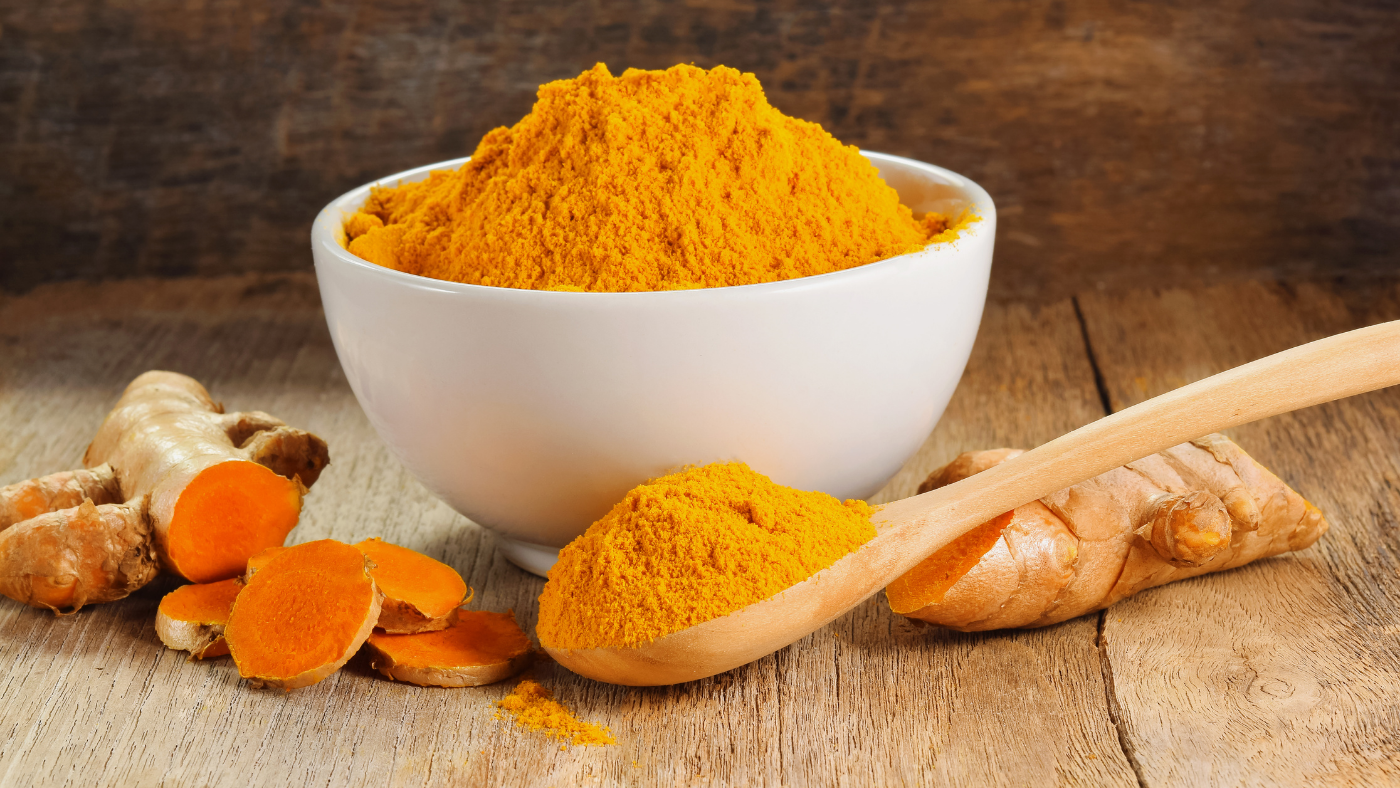 ground turmeric in a bowl surrounded by a spoon of turmeric and turmeric slices