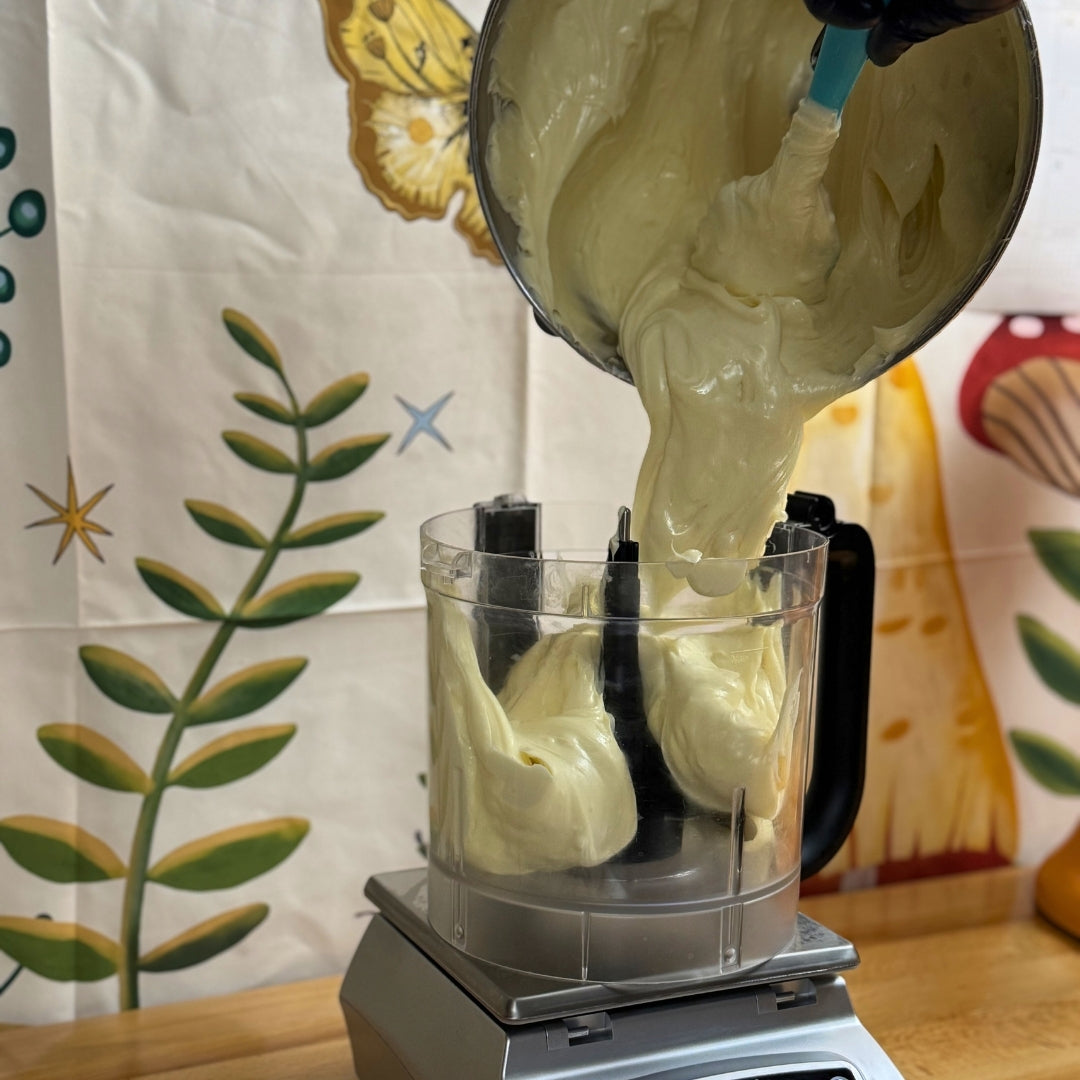 tallow cream being poured from a bowl into a food processor with a decorative kitchen towel in the background.