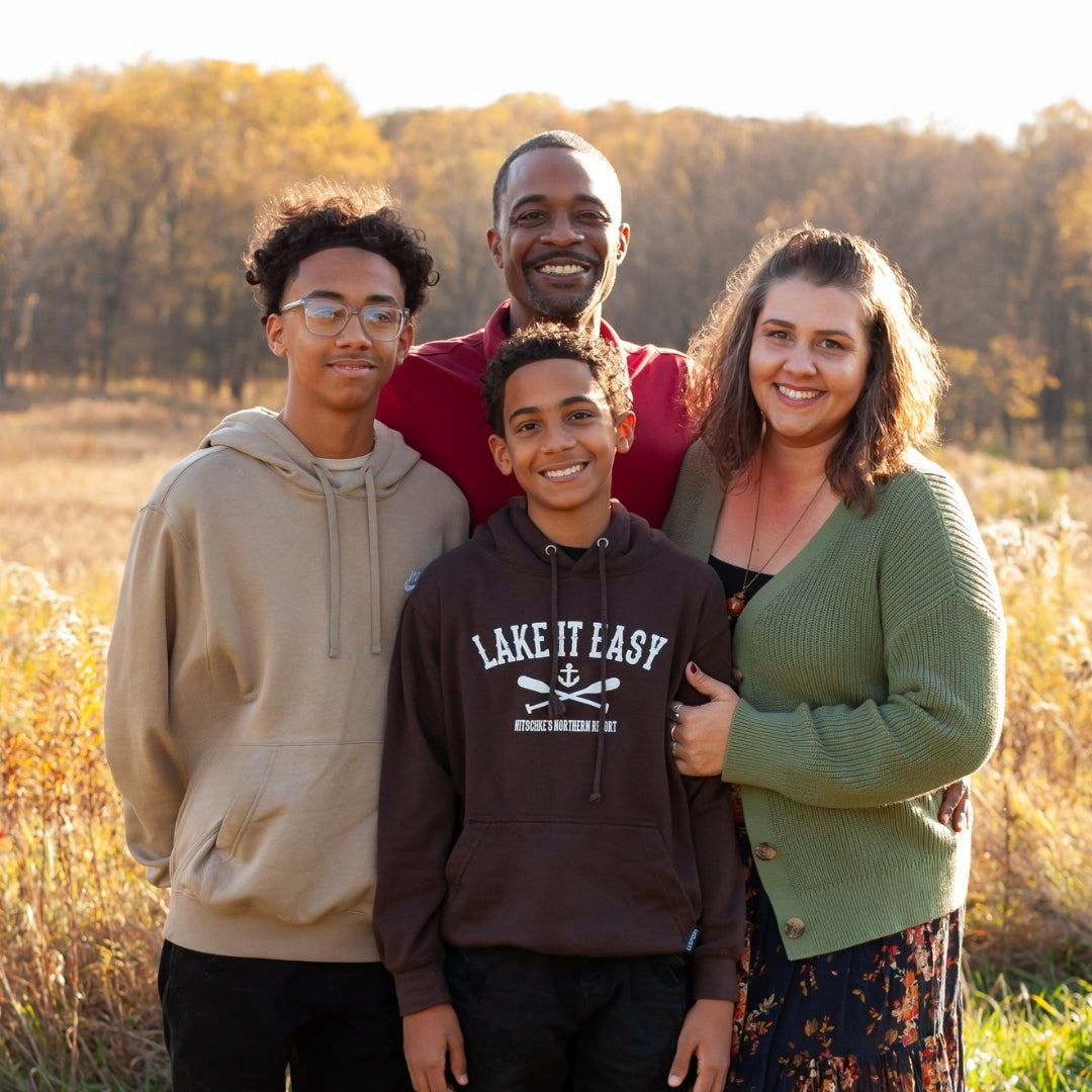Family of four standing in a field with trees in the background