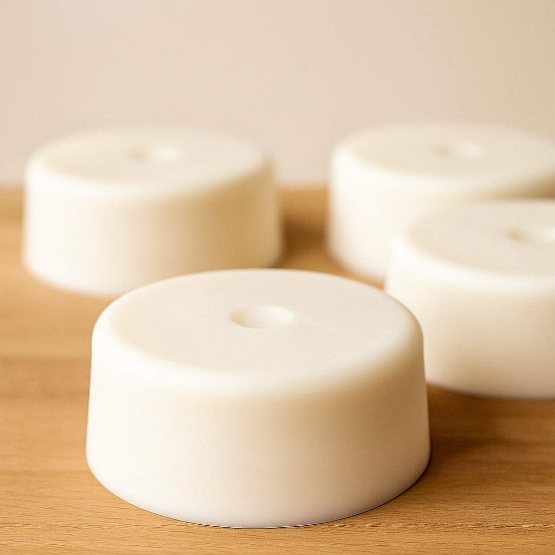 Three white cylindrical bricks of grass fed tallow on a wooden surface with a blurred background