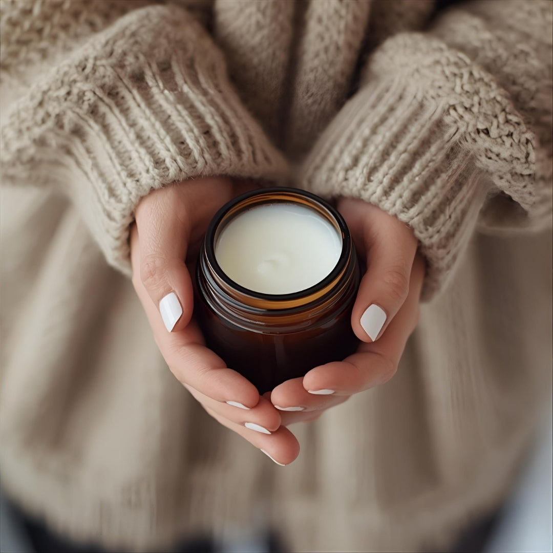 hand holding a jar of grass fed tallow moisturizer by Nefertem with cozy sweater on